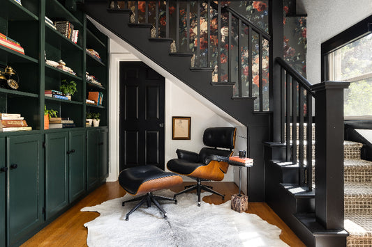 Green Floral Wallpaper in staircase with modern interior with dark green bookshelves and black and orange chair.