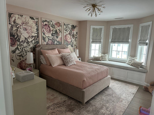 Light floral wallpaper in panels behind a bed with pillows, and a window seat.