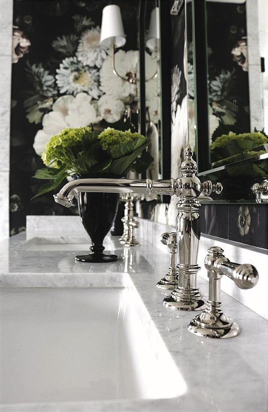 Bathroom sink with ornate silver faucet and mirror with floral wallpaper on the wall.