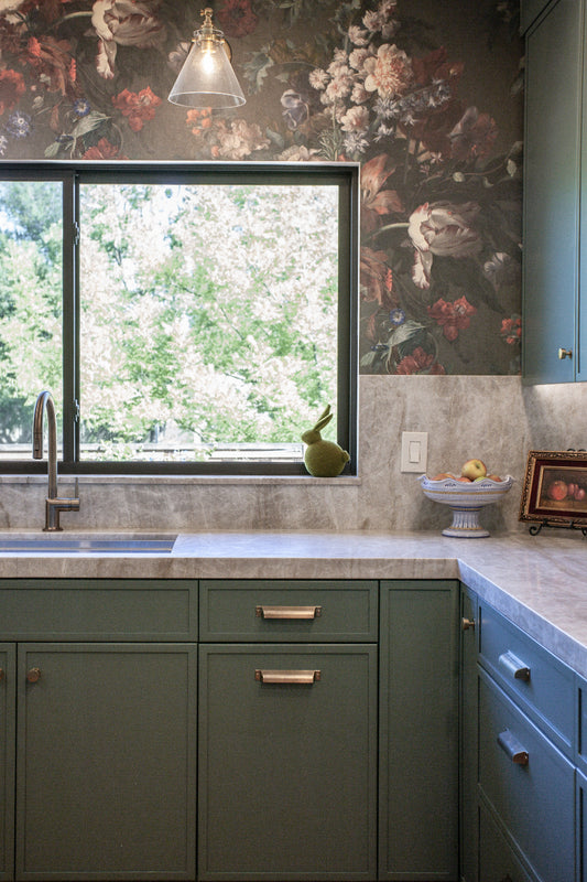 Floral Wallpaper in kitchen with green cabinets, marble counter top, and a window view.
