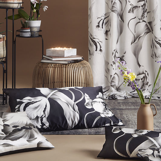 Cushions and curtain with black and white twisting tulips floral design with a decorative vase and books in the background.